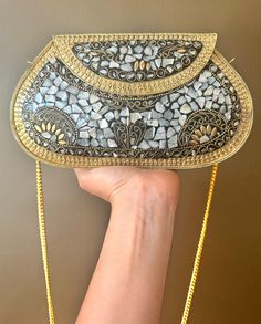 Dive into the opulence of handcrafted elegance with this stunning mosaic clutch, a treasure designed to add a touch of glamour to your ensemble. Each piece of this exquisite accessory has been carefully assembled to create a dazzling spectacle of light and texture. Features: Material Brilliance: This clutch boasts a breathtaking array of iridescent mother-of-pearl pieces, intricately laid to form a mosaic that captures and reflects light with every movement. The natural hues of the shell ensure that no two clutches are exactly alike, giving you a one-of-a-kind fashion statement. Golden Glow: Surrounding the shell inlays is a frame of radiant gold-tone metalwork, featuring delicate filigree and beaded details that echo the luxury of vintage artistry. Versatile Carry: Accompanied by a sleek Bohemian Embellished Clutch As Gift, Sequin Clutch Evening Bag As Gift, Sequin Clutch Evening Bag For Gifts, Gold Bohemian Clutch For Formal Events, Bohemian Gold Clutch For Formal Occasions, Elegant Festive Sequined Clutch, Rectangular Sequined Clutch As Gift, Bohemian Embellished Clutch For Gift, Festive Silver Beaded Evening Bag