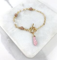 "- Bracelet Size: Length: 7.5 | Paper Clip Chain Thickness: 2.6 mm Beige Balls Width: 6.1mm | Clear Ball Width: 4.5mm Drop Hand Height: 0.9 inches Toggle Closure: 0.5 Inches and 0.7 Inches 18K Gold Filled Beige Beads and Pink Hand Charm Bracelets Featuring Toggle Clasp And Link Chain For Wholesale and Jewelry Supplies 💎 With new products daily, quality and competitive prices, in DiJu Jewelry you find the most unique styles of modern designs, always looking for elegance and market trends. *Helpi Gold Crystal Bracelet With Beaded Chain For Gift, Gold Beaded Dangle Charm Bracelet, Elegant Beaded Toggle Necklace As Gift, Gold Toggle Necklace With Round Beads, Gold Beaded Toggle Necklace With Round Beads, Elegant Beaded Toggle Necklace For Gifts, Toggle Necklace With Round Beads For Gifts, Toggle Clasp Necklace With Round Beads, Gold Toggle Necklace With Round Beads As A Gift