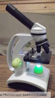 a microscope sitting on top of a wooden table next to a green ball and black object