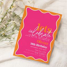 an orange and pink birthday party card on a white sheet with flowers in the background