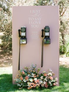 two old fashioned telephones sitting on top of a pink sign with flowers in front of it