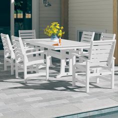 a white table and chairs next to a swimming pool with flowers in the vase on top