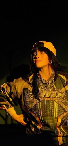 a woman with long hair wearing a yellow hat and striped shirt standing in the dark