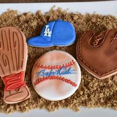 three decorated cookies in the shape of baseballs and mitts on top of sand