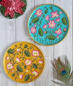 two plates with flowers painted on them next to a peacock feather and flower potted plant