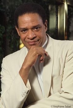 a man in a white suit and tie posing for the camera with his hand on his chin