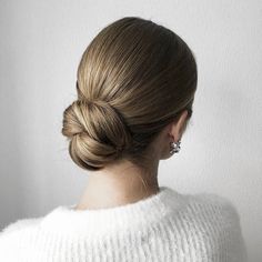 a woman with her hair in a low bun, wearing a white sweater and earrings