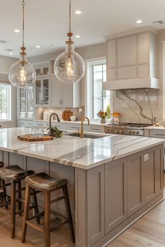 a large kitchen island with stools and lights hanging from it's ceiling above