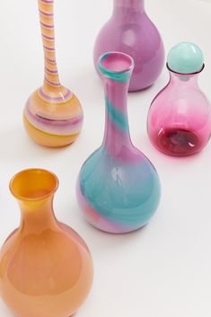 four different colored vases sitting next to each other on a white surface with no one around them