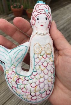 a hand holding a little mermaid doll in it's right hand and wearing a pearl necklace