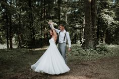 a bride and groom walking through the woods