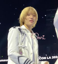 a male in a white jacket and some confetti around his neck, standing on stage