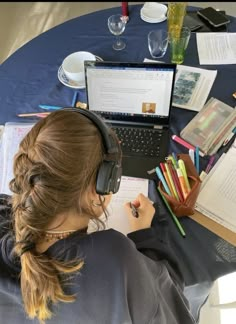 a woman wearing headphones sitting at a table with a laptop and books on it