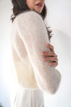 a woman wearing a white sweater and holding her arm around her neck while looking off to the side