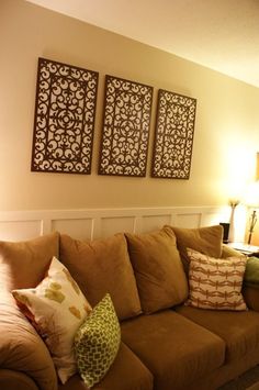 a living room with brown couches and three decorative wall art on the wall above them