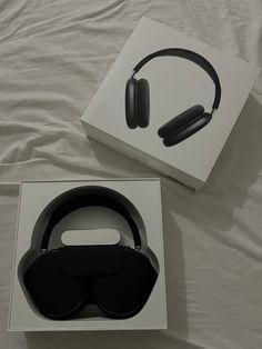 an open box with headphones in it sitting on a white sheeted bed next to a pair of black ear phones