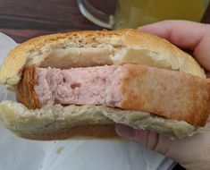 a person holding a half eaten sandwich with meat in it's center and bread on the other side