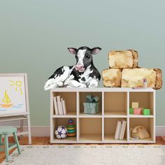 a black and white cow sitting on top of a shelf next to a book case