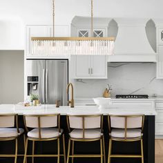 a kitchen with white cabinets and marble counter tops, gold accents on the pendant lights over the island