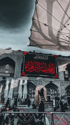 an arabic sign on the side of a building with people sitting under it and umbrellas