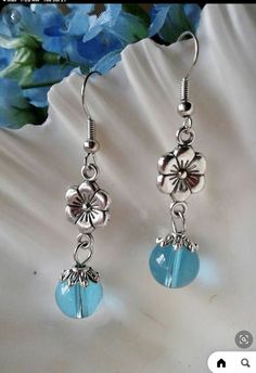 a pair of earrings with blue beads and flowers on them sitting next to a flower