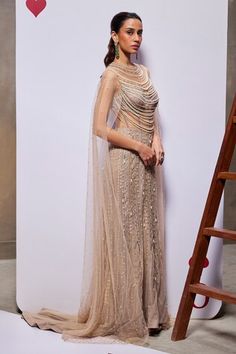 Beige gown heavily embellished with intricate pearl tassels and longline cape sleeves. - Aza Fashions Hand Embellished Floor-length Evening Dress For Reception, Festive Floor-length Hand Embellished Evening Dress, Festive Hand Embellished Floor-length Evening Dress, Embellished Floor-length Gown For Reception, Festive Floor-length Evening Dress With Sheer Dupatta, Hand Embellished Floor-length Gown For Reception, Hand Embellished Maxi Evening Dress For Reception, Hand Embellished Maxi Length Evening Dress For Reception, Glamorous Floor-length Gown For Reception