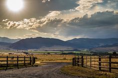 the sun shines brightly over an open field with mountains in the background and a dirt road running through it