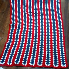 a red, white and blue crocheted blanket laying on top of a wooden floor