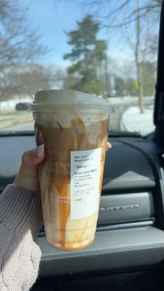 a woman holding up a cup of iced coffee in her hand while sitting in the passenger seat of a car