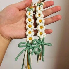 a hand holding two white and green crocheted bracelets with yellow flowers on them