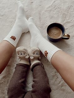 two people wearing white socks with monkey faces on them and one has their feet crossed, while the other is holding a cup of coffee