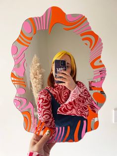 a woman taking a selfie with her cell phone in front of a colorful mirror