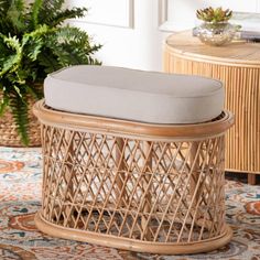 a wicker ottoman with a cushion on it in front of a potted plant