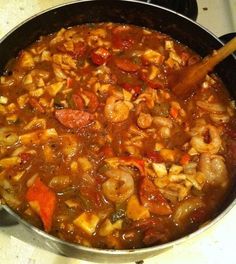 a pot filled with shrimp and vegetables on top of a stove next to a wooden spoon