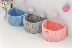 three knitted baskets sitting next to each other in front of a white brick wall