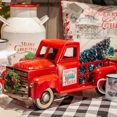 an old red truck with christmas decorations on the bed in front of it and coffee mugs next to it