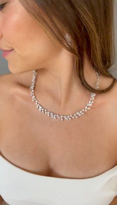 a woman in a white dress wearing a silver necklace and earring with pearls on it