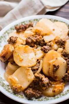 a white plate topped with potatoes and meat covered in sauce on top of a wooden table