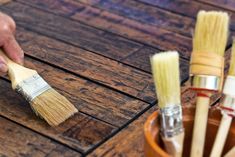 a person holding a paint brush near some brushes in a wooden container on a table