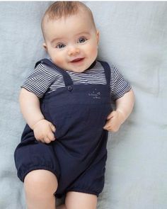 a baby laying on top of a bed wearing a blue bib and overalls