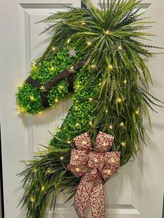 a christmas wreath with lights hanging on the front door, decorated with evergreen and red bows