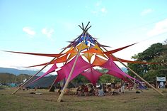 a group of people sitting around a large colorful structure in the middle of a field