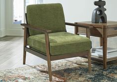 a green chair sitting on top of a rug next to a wooden table and lamp