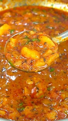 a ladle full of soup being held by a wooden spoon