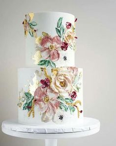 a three tiered cake with flowers painted on the side and gold leaf decoration around the edges