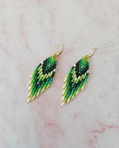 two green and white beaded earrings sitting on top of a marble counter next to each other