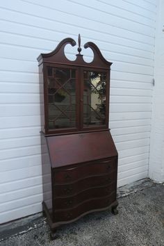 an old wooden desk sitting in front of a white building with a window on top