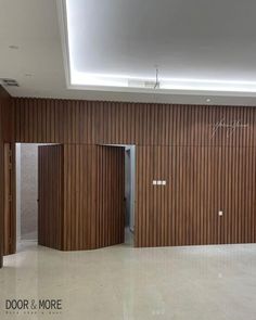 an empty room with wooden slats on the wall and two open doors leading to another area