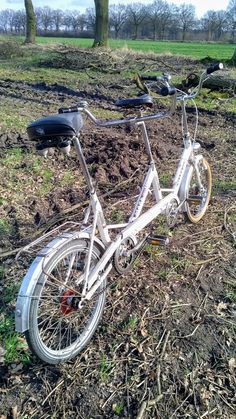 an old bicycle sitting in the middle of a field with trees and grass behind it