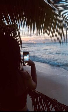 a woman taking a photo with her cell phone on the beach at sunset or dawn